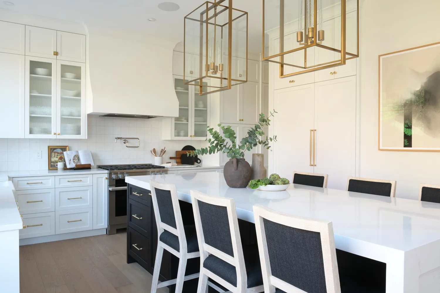 textural details in kitchen: brass lighting, upholstered chairs, quartz countertop, plaster range hood, and painted wood cabinetry